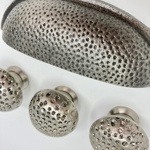 以下が含まれることがあります： 表面がざらざらしていて、くぼみのある銀色のキャビネットノブが3つあります。ノブは丸く、わずかにドーム型をしています。同様のざらざらした表面を持つ銀色のキャビネットプルも表示されています。