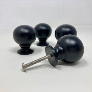 May include: Four black round cabinet knobs with a silver screw. The knobs have a smooth, slightly shiny finish.
