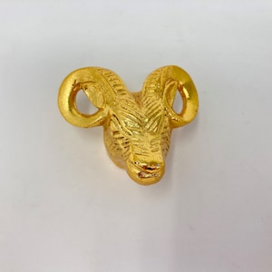 May include: A gold-coloured metal ram's head sculpture with detailed horns and a textured surface.