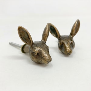 以下が含まれることがあります： アンティークゴールドのウサギの頭の形をしたキャビネットノブ2個。背面にネジが付いています。