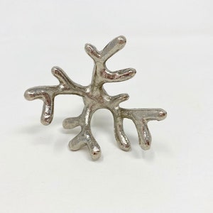 Puede incluir: Anillo para servilletas de metal plateado con forma de rama de coral.