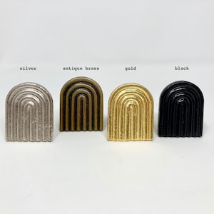 Può includere: Quattro tiretti per cassetti in metallo arcuati in diverse finiture: argento, ottone anticato, oro e nero.