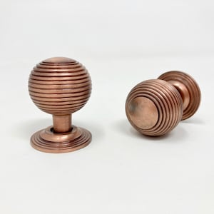 May include: Two copper cabinet knobs with a ribbed design. The knobs are round and have a base.