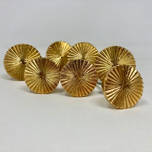 May include: Six gold-toned round cabinet knobs with a sunburst design. The knobs have a raised, textured surface.