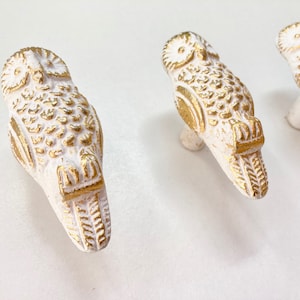 以下が含まれることがあります： 金色のアクセントが付いた白いフクロウの形をしたキャビネットノブが3つ。フクロウは羽根が細かく、丸い目のデザインです。