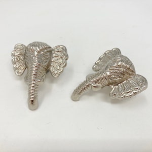 May include: Two silver elephant-shaped drawer pulls with detailed carvings.