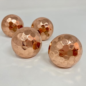 May include: Four copper-coloured round cabinet knobs with a hammered texture.