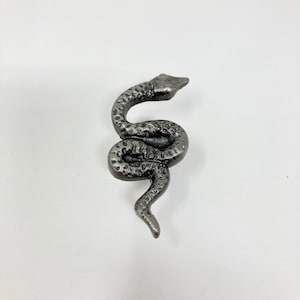 Könnte beinhalten: Eine silberne Schlangenfigur aus Metall mit einer strukturierten Oberfläche. Die Schlange ist zu einer Spirale zusammengerollt, mit dem Kopf nach oben.