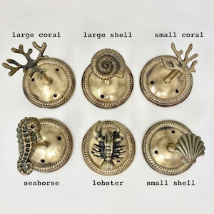 May include: Six brass hooks with different sea life designs. The hooks are round and have a decorative border. The designs include a large coral, a large shell, a small coral, a seahorse, a lobster, and a small shell.