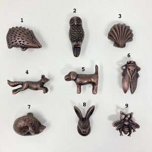 May include: Set of ten bronze-colored animal and nature-themed drawer pulls. The pulls feature a hedgehog, owl, seashell, fox, dog, rabbit, cat, dragonfly, and two bees.