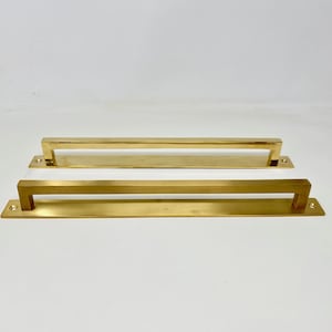 May include: Two gold-toned metal cabinet pulls with a rectangular shape. The pulls are approximately 30 cm long and have a slightly brushed finish.