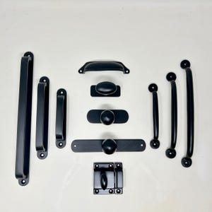 May include: A selection of black cabinet hardware, including handles, pulls, and a latch. The hardware features various shapes and sizes, with a matte finish. The arrangement showcases a range of design options for furniture and cabinetry.