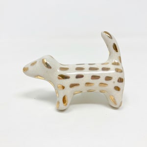 May include: White ceramic dog figurine with gold spots. The dog is standing on all four legs with its tail curled up.