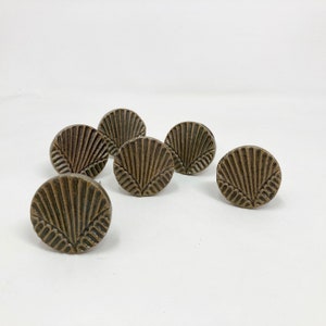 Pode incluir: Seis botões de armário de cerâmica marrom com um design em forma de leque. Os botões têm um acabamento desgastado e são perfeitos para adicionar um toque de charme rústico a qualquer casa.