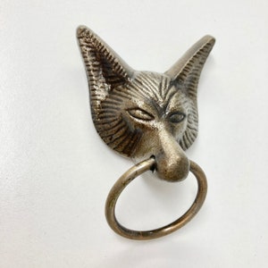 May include: A silver fox head door knocker with a brass ring. The fox has a detailed face with a furrowed brow and a slightly open mouth.