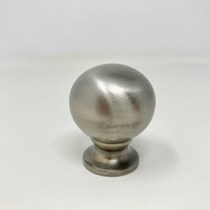 Könnte beinhalten: Ein silberner Metallknopf mit runder Oberseite und einer kleineren Basis. Der Knopf hat eine gebürstete Oberfläche.