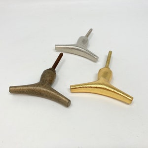 Puede incluir: Tres pomos de armario de metal diferentes en forma de Y. Los pomos son plateados, dorados y bronce.