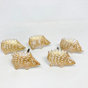 Könnte beinhalten: Vier goldfarbene Keramik-Schubladengriffe in Form von Igeln mit weißen Akzenten. Die Igel sind nach rechts gerichtet und haben eine strukturierte Oberfläche.