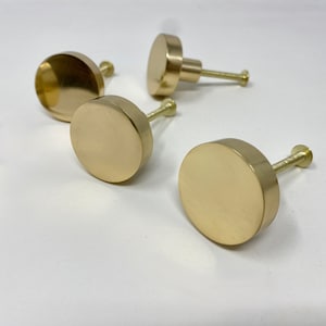 Peut inclure: Quatre boutons ronds en or pour armoire avec une fixation à vis. Les boutons sont lisses et ont une finition polie.