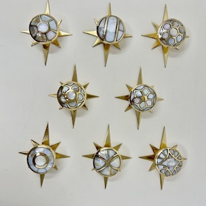 May include: Nine brass starburst decorative accents with mother-of-pearl centers. Each starburst has a unique design in the center, with a gold finish and pointed rays extending outwards. The mother-of-pearl has a pearlescent sheen.