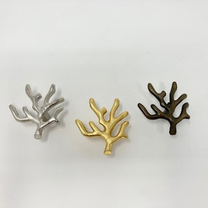 Puede incluir: Tres tiradores de cajón de metal con forma de coral en plata, oro y bronce.