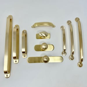 May include: A set of ten gold-toned cabinet hardware pulls and knobs. The set includes a variety of styles, including bar pulls, cup pulls, and knobs. The hardware is made of metal and has a polished finish.