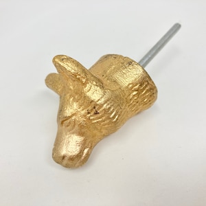 Op de afbeelding: Gouden metalen dierenkop-kastknop met een schroef. De dierenkop is gestileerd en lijkt op een vos of een wolf.