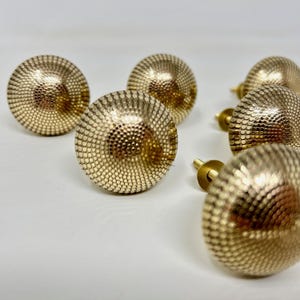 May include: Six gold-toned cabinet knobs with a textured, circular design. Each knob has a small screw for attaching to a cabinet door.