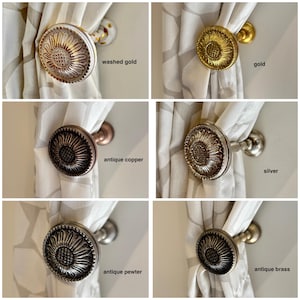 Può includere: Una collezione di fermatende decorative in varie finiture, tra cui oro anticato, oro, rame antico, argento, peltro antico e ottone antico. Ogni fermatenda presenta un design a girasole.