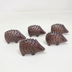 Könnte beinhalten: Fünf kleine, braune, keramische Schubladenknöpfe in Form eines Igels. Jeder Knopf ist mit einer strukturierten, stacheligen Rückseite und einer glatten, abgerundeten Vorderseite verziert.