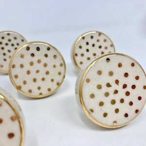 May include: Set of five white ceramic cabinet knobs with gold polka dots and a gold rim.
