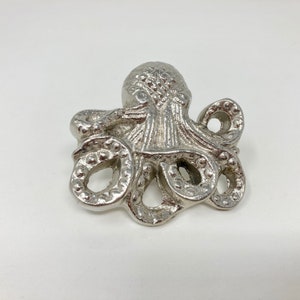 Puede incluir: Una figurita de pulpo de plata con tentáculos detallados y un cuerpo texturizado.