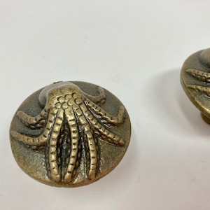 May include: Two antique brass octopus drawer pulls. The octopus is raised and detailed with textured tentacles.