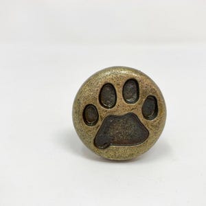 Puxador de gaveta em latão antigo com formato de pata de cachorro ou gato.