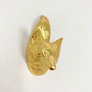Pode incluir: Um gancho de parede em forma de cabeça de raposa de cor dourada. O gancho é feito de metal e tem um design realista de cabeça de raposa. Os olhos da raposa são pretos e o nariz é pontudo.