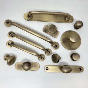 Könnte beinhalten: Eine Sammlung antiker Messing-Schrankbeschläge, darunter Griffe, Knöpfe und ein Türgriff. Die Beschläge sind in verschiedenen Formen und Größen, darunter rund, oval und rechteckig.