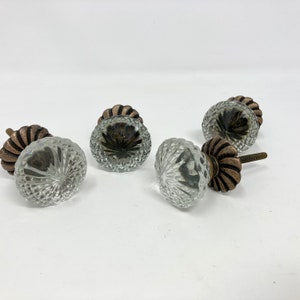 Op de afbeelding: Vier heldere glazen kastknoppen met een facetgeslepen ontwerp en een koperkleurige metalen basis.