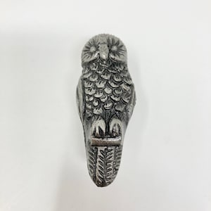 May include: A silver metal owl figurine with detailed feathers and large eyes. The owl is standing upright with its wings folded.