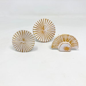 Peut inclure: Trois boutons en céramique blanche avec un motif soleil doré. Les boutons sont ronds et ont un design en relief.