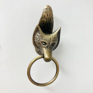 Könnte beinhalten: Ein goldfarbener Türklopfer in Form eines Fuchs Kopfes mit einem Ring zum Ziehen. Der Fuchs hat ein detailliertes Gesicht mit schwarzen Augen und einem strukturierten Fellmuster.