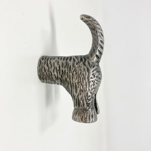 May include: A silver metal dachshund dog hook. The hook is shaped like a dachshund dog with its tail curled up. The dog is textured to look like fur.