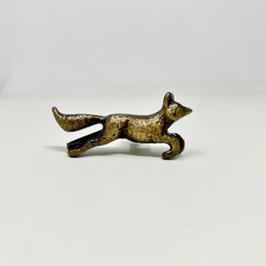 Peut inclure: Une figurine de renard en métal doré dans une pose de course. Le renard a une surface texturée détaillée et une longue queue touffue.