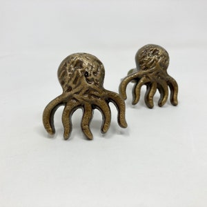 May include: Two gold-toned octopus-shaped drawer pulls. The octopus has a detailed, textured surface.