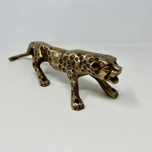 Könnte beinhalten: Eine goldfarbene Metallfigur eines Geparden mit gepunktetem Muster in geduckter Haltung.