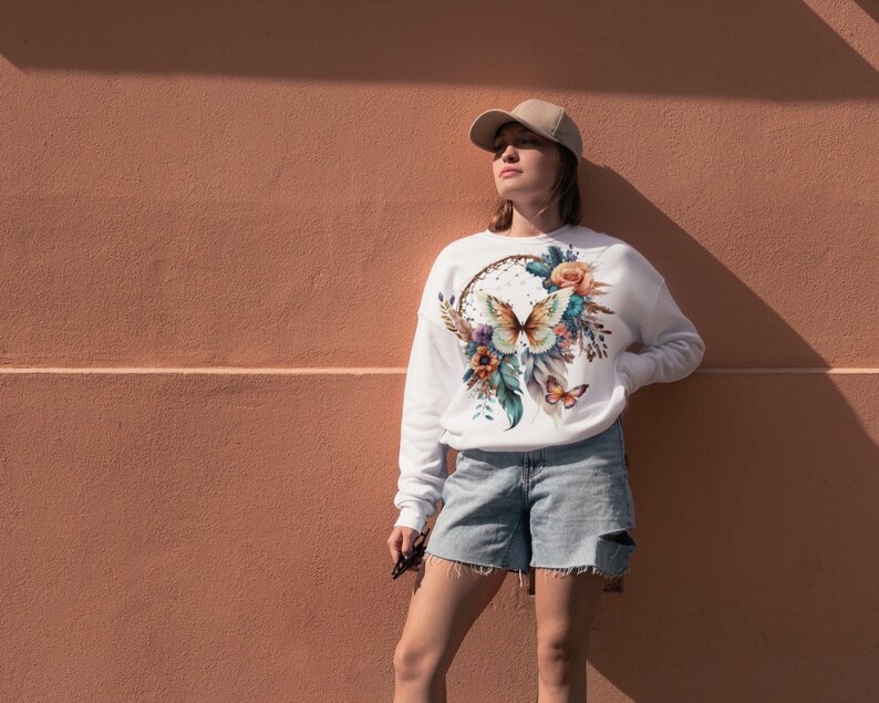 May include: White sweatshirt with a colorful butterfly and floral design on the front. The design features a dreamcatcher with feathers and flowers.