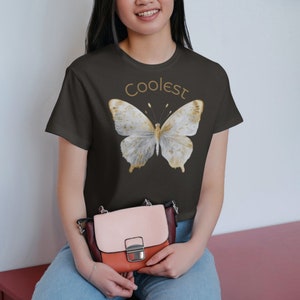 May include: A dark gray t-shirt with a white butterfly graphic and the text "Coolest" in gold lettering.