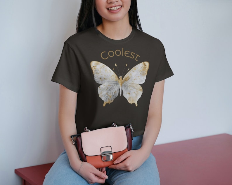 May include: A dark gray t-shirt with a white butterfly graphic and the text "Coolest" in gold lettering.