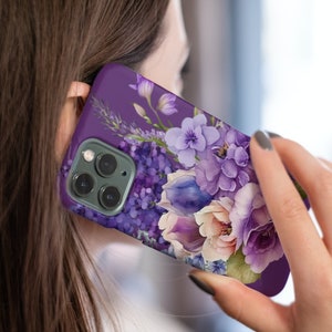May include: Purple phone case with a floral design featuring a bouquet of purple, white, and pink flowers. The case has a camera lens cutout.