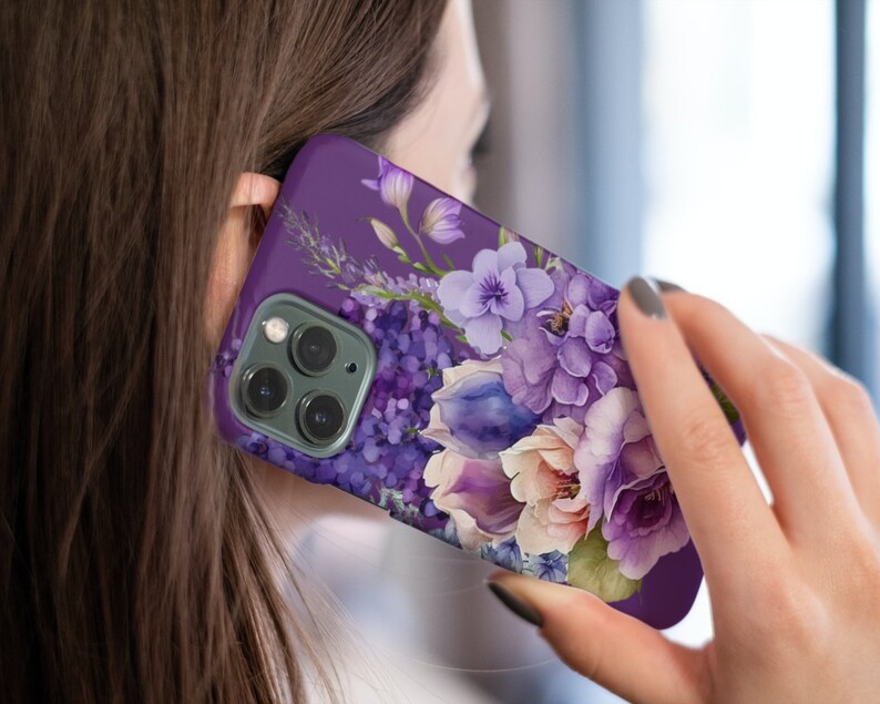May include: Purple phone case with a floral design featuring a bouquet of purple, white, and pink flowers. The case has a camera lens cutout.
