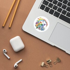 May include: A watercolor sticker featuring a butterfly with rainbow wings and flowers. The butterfly is perched on a rainbow arc. The sticker is on a white background.